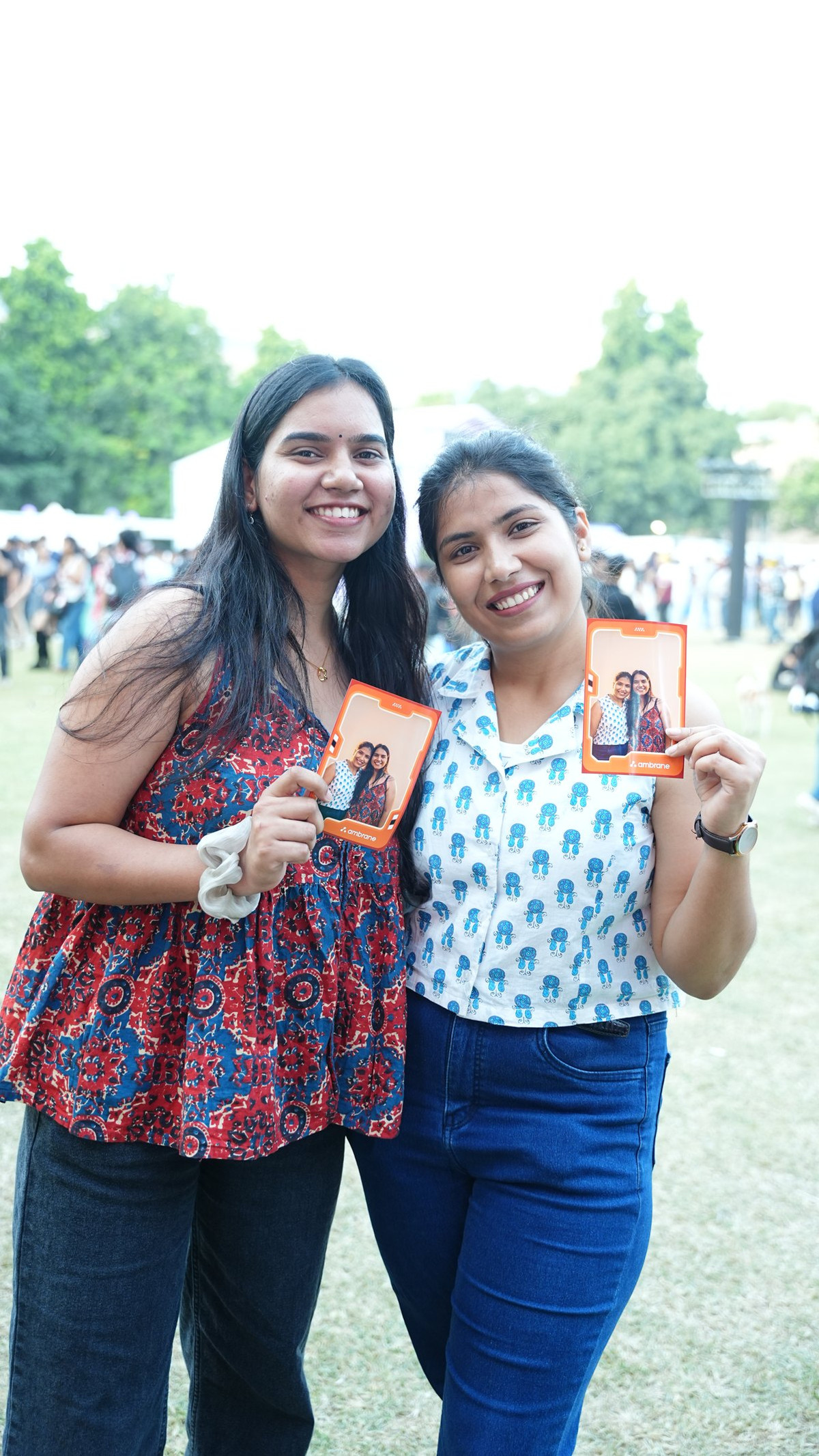 Two young women smiling and holding up their printed photos from a Pikcha AI photo booth at an outdoor event