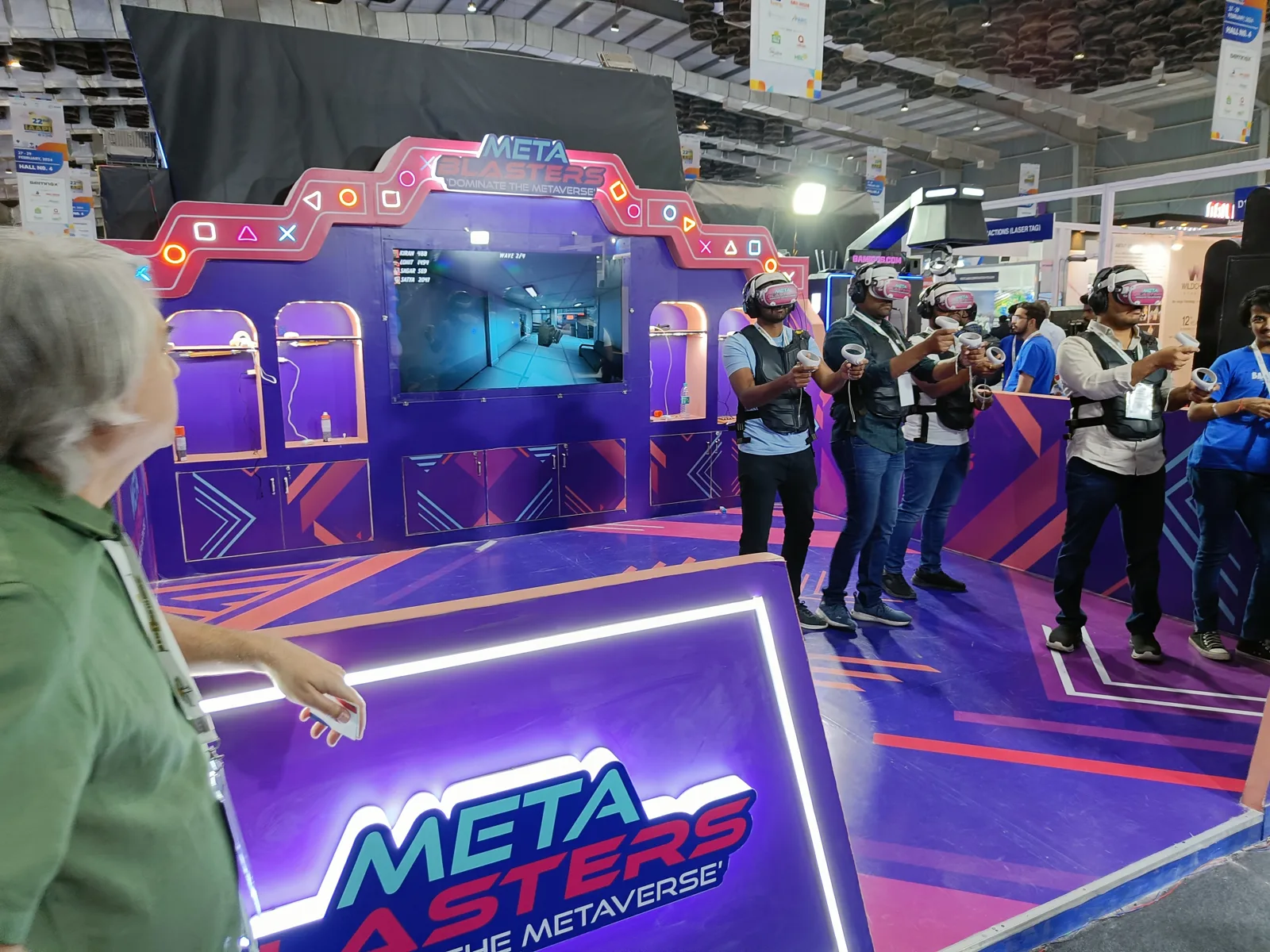 Neon lit META BLASTERS stand at an expo hall with visitors