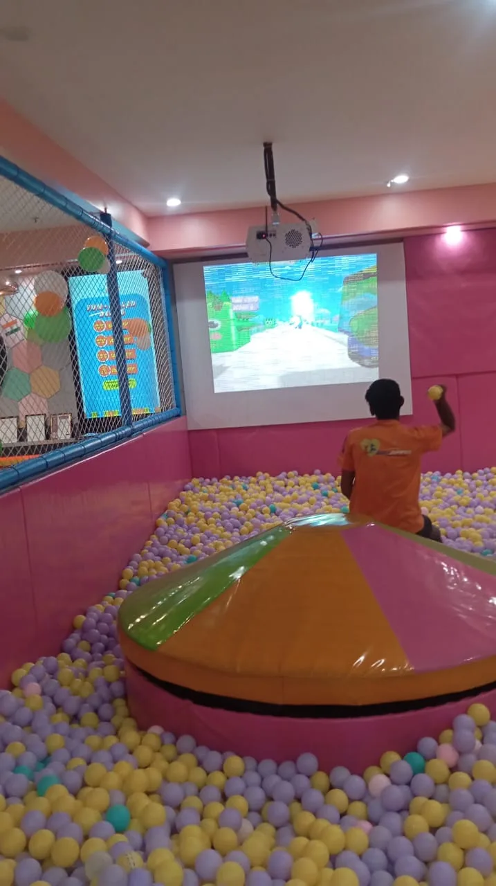 Child in a ball pit facing a pink wall projection game