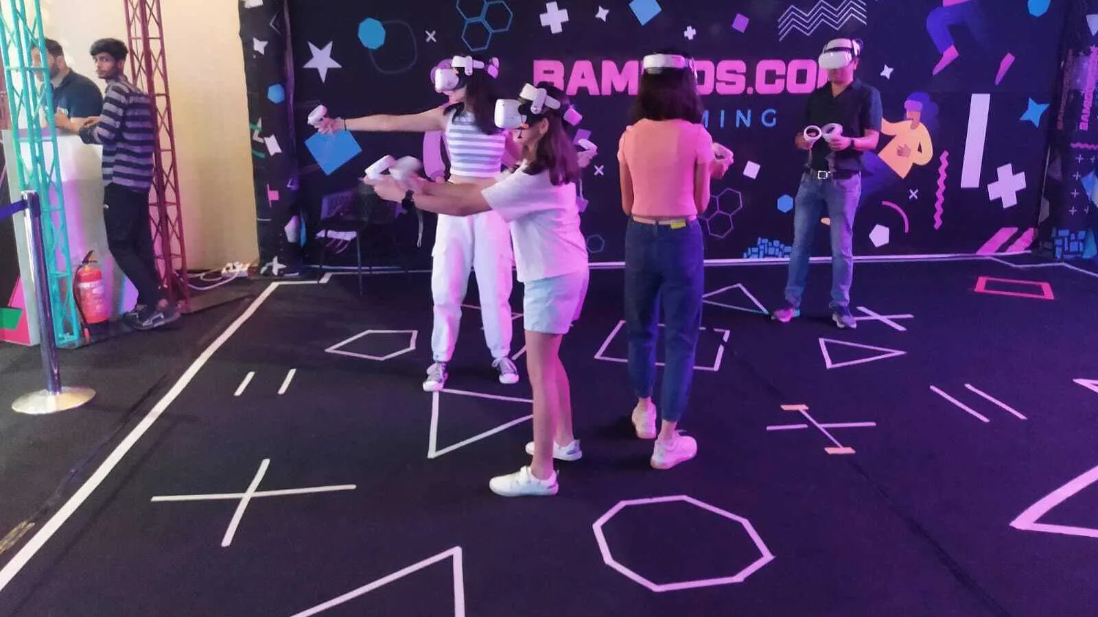 Players in VR headsets aiming controllers inside the arena with the BAMIGOS.COM GAMING wall