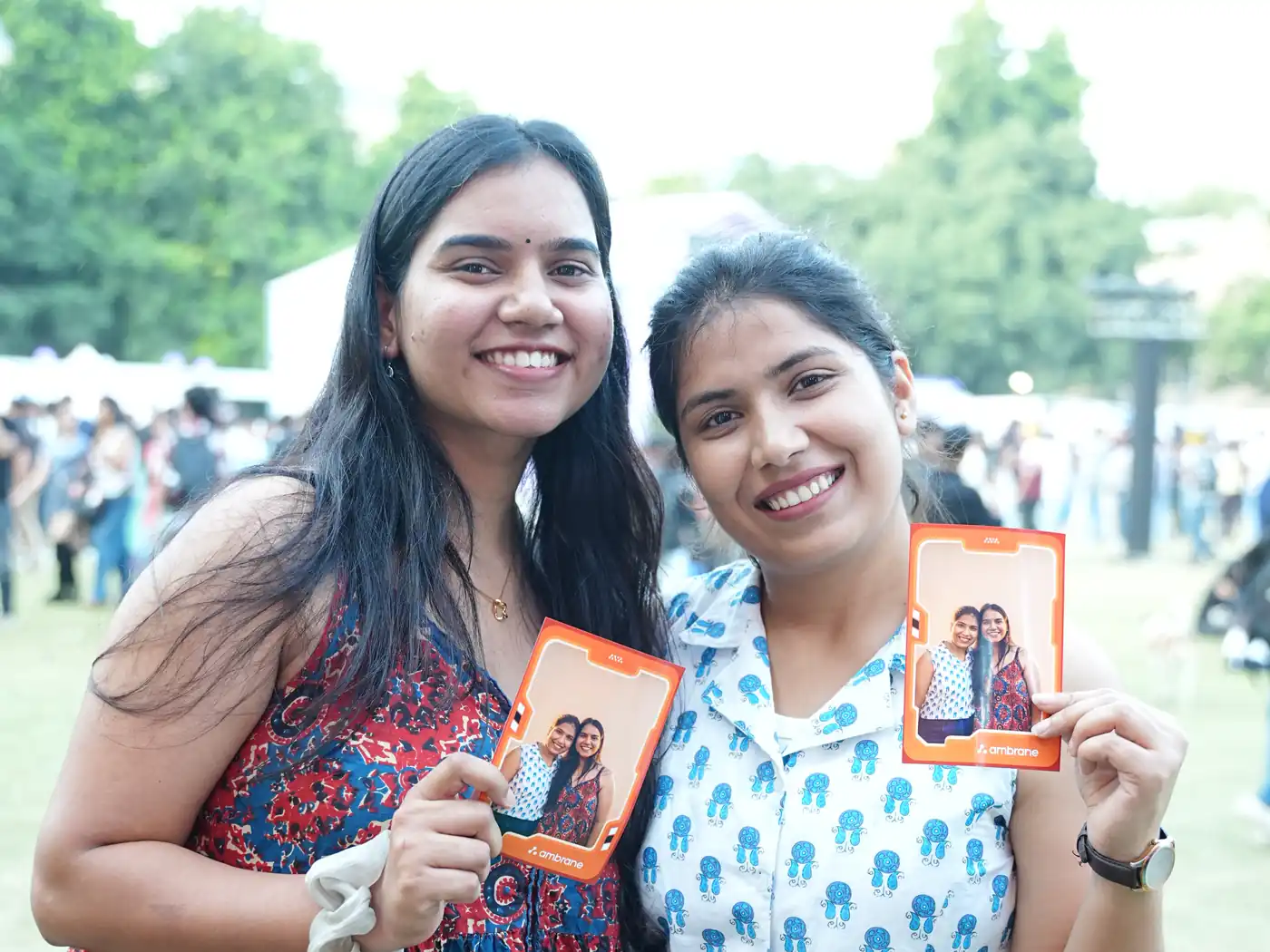 Two friends smiling with their AI photo booth prints at a college fest