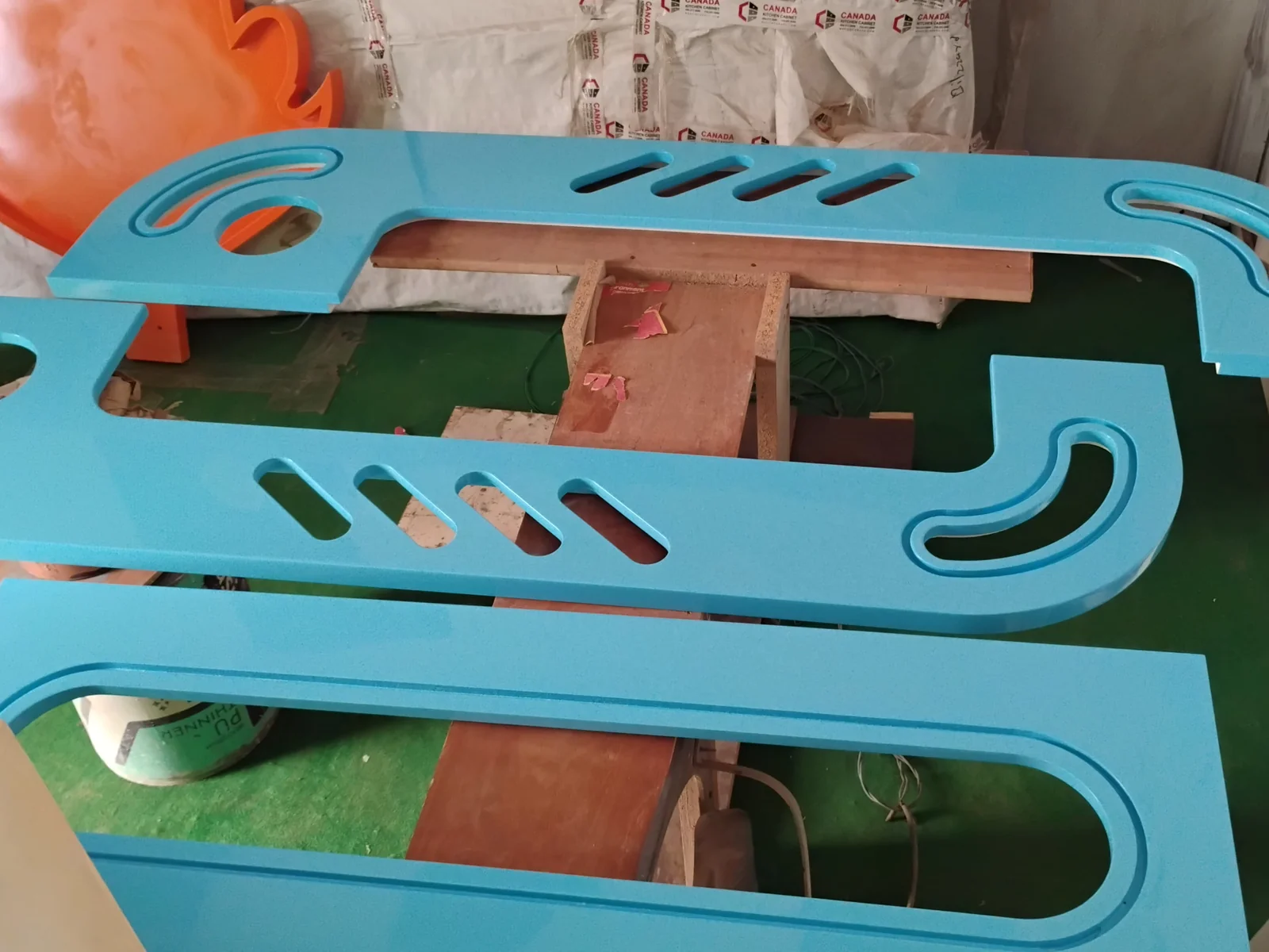 Glossy blue painted cabinet side panels with slots, laid out to dry