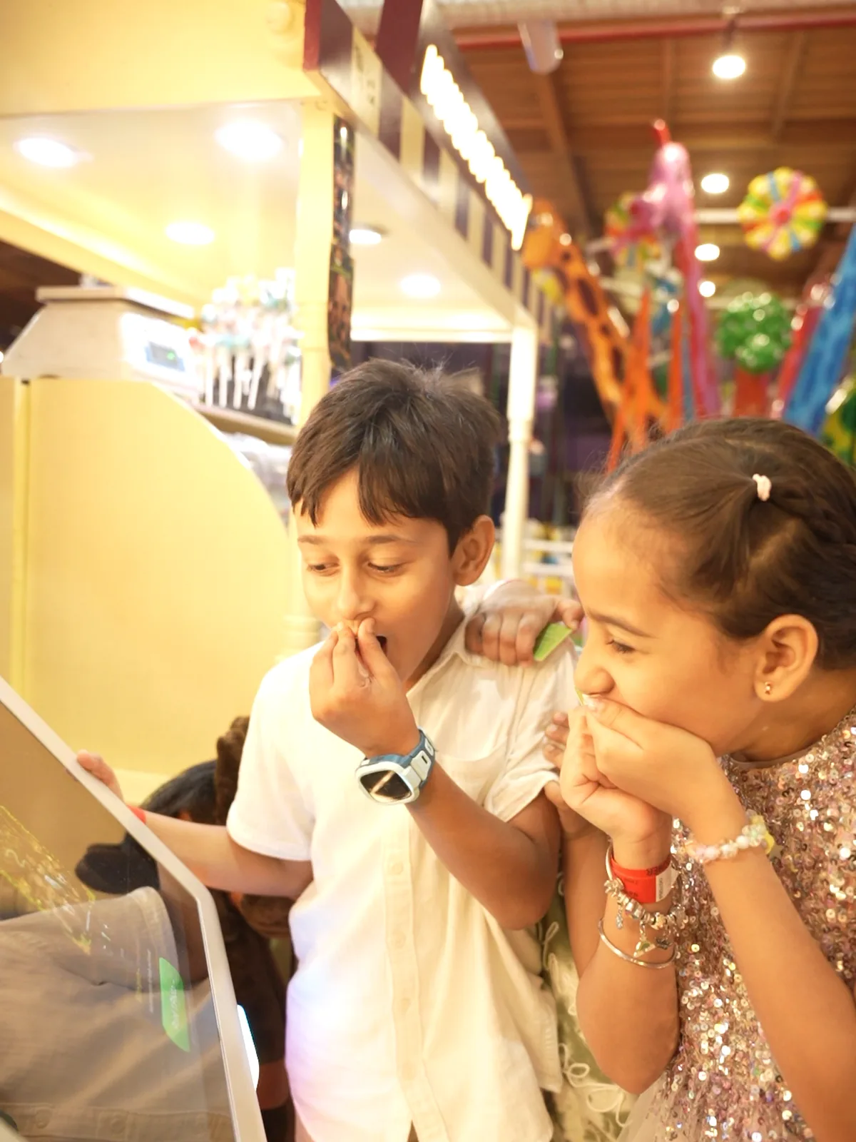 Two kids laughing with their hands over their mouths at the Pikcha photo booth screen at Boombastic in Gurugram