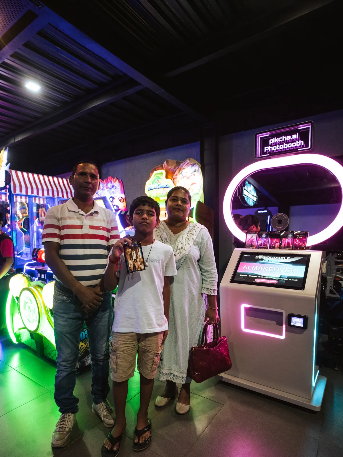 Family of three with a fresh print next to the Pikcha photo booth in a gaming arcade