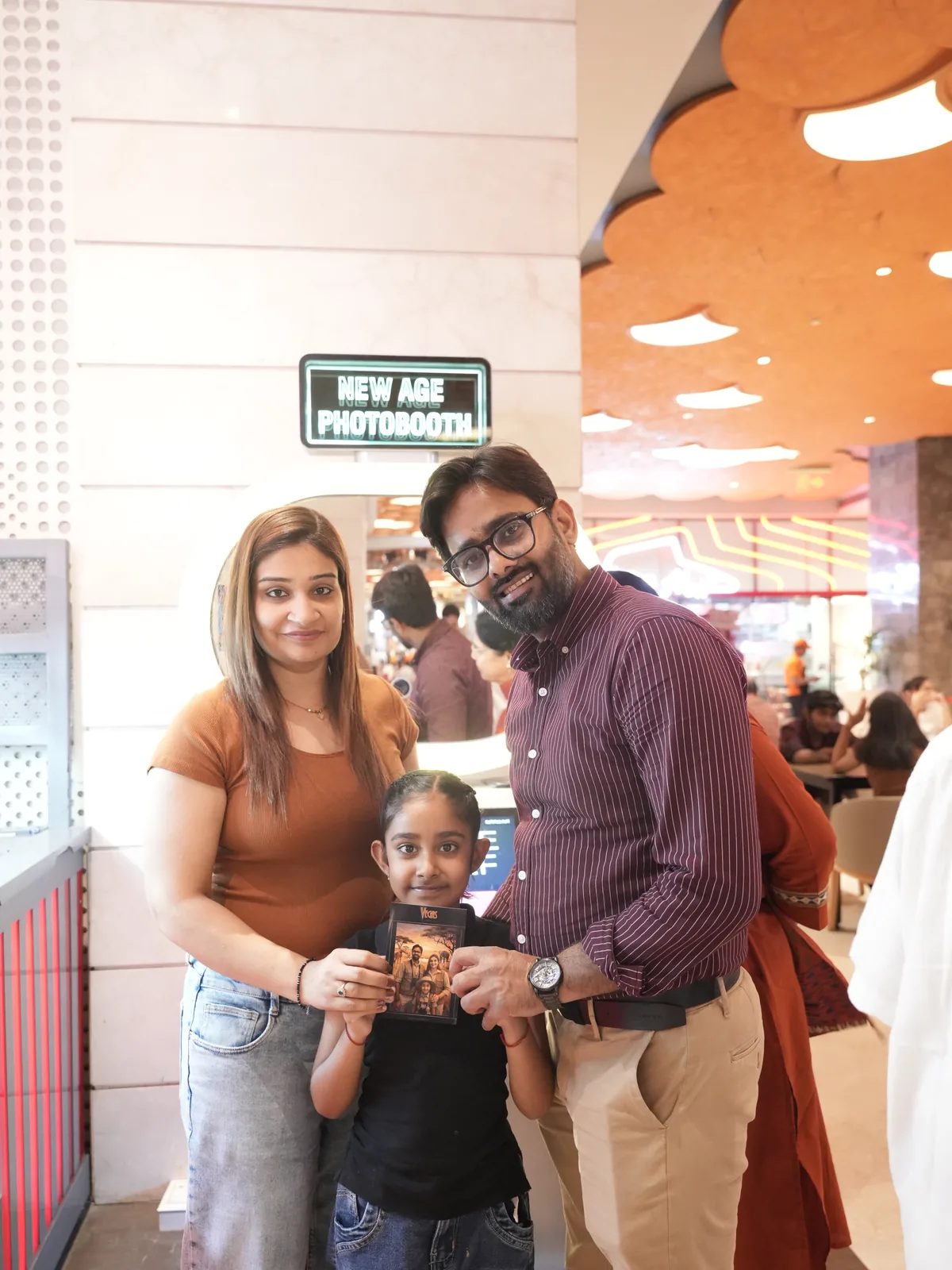 Mother, father and daughter smiling with the prints they just took at a Pikcha photo booth