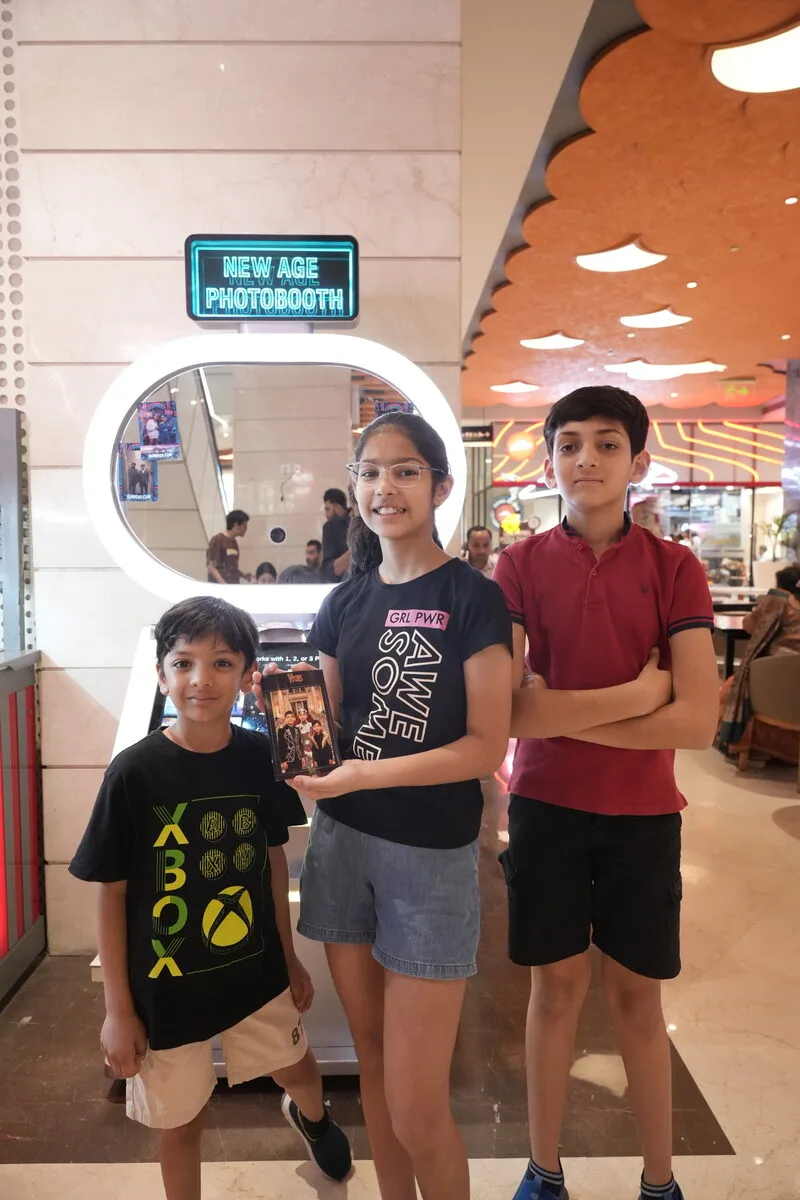 Three kids posing with their print at the Pikcha AI Photo Booth in a mall