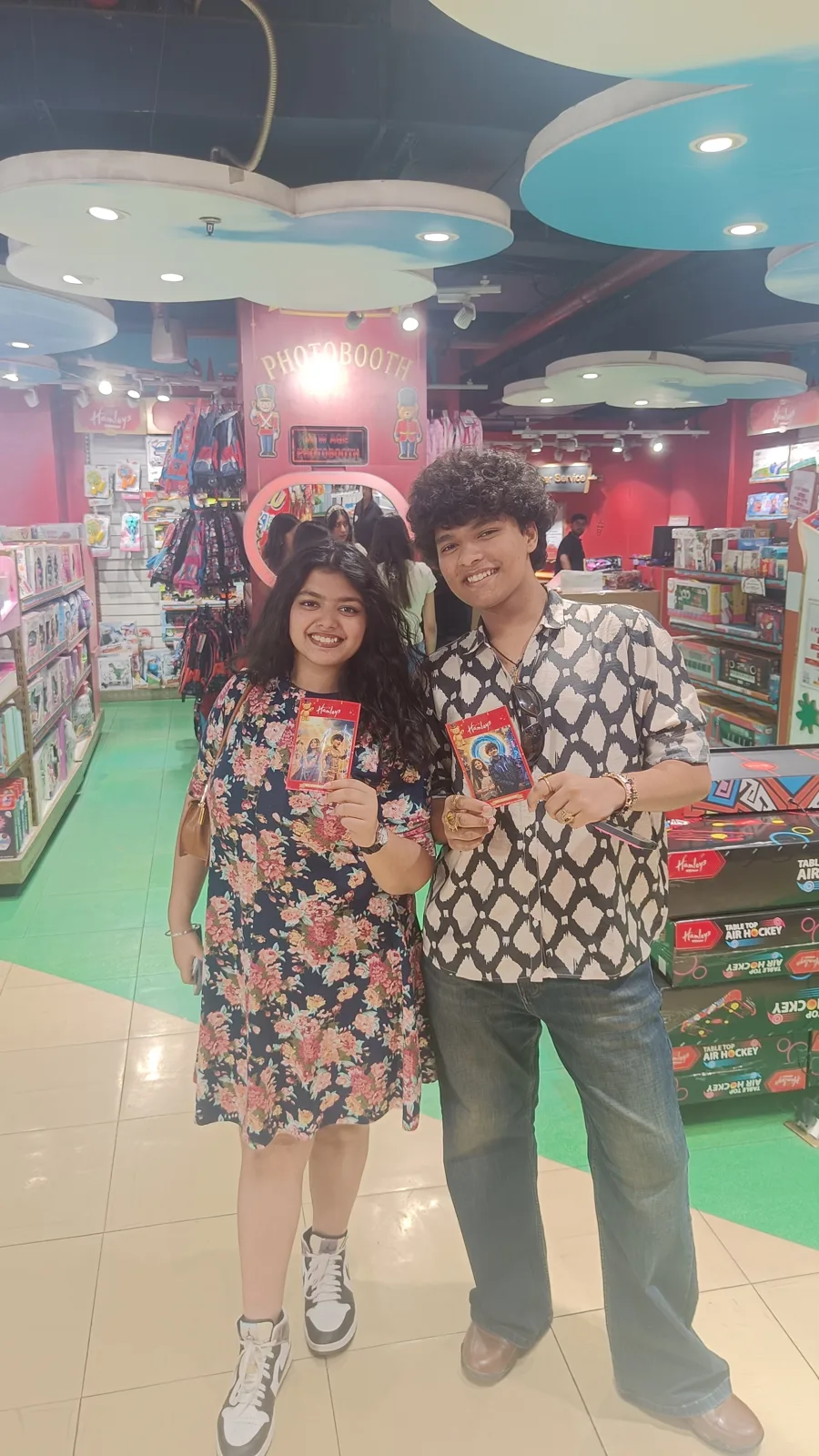 Two guests with their prints beside the red Pikcha booth at Hamleys